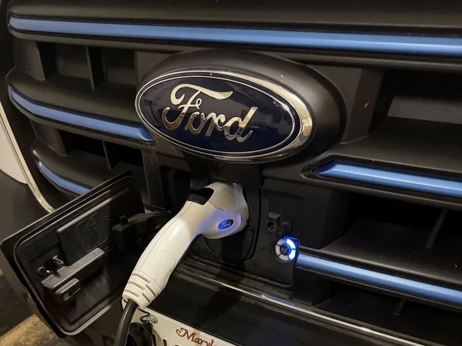 A charging connector plugged into the port below the Ford badge on an Eagle Transit van, its indicator ring lit.