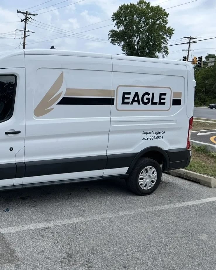 An Eagle Solutions electric cargo van in white and tan livery, parked on a lot in the Washington, DC area.